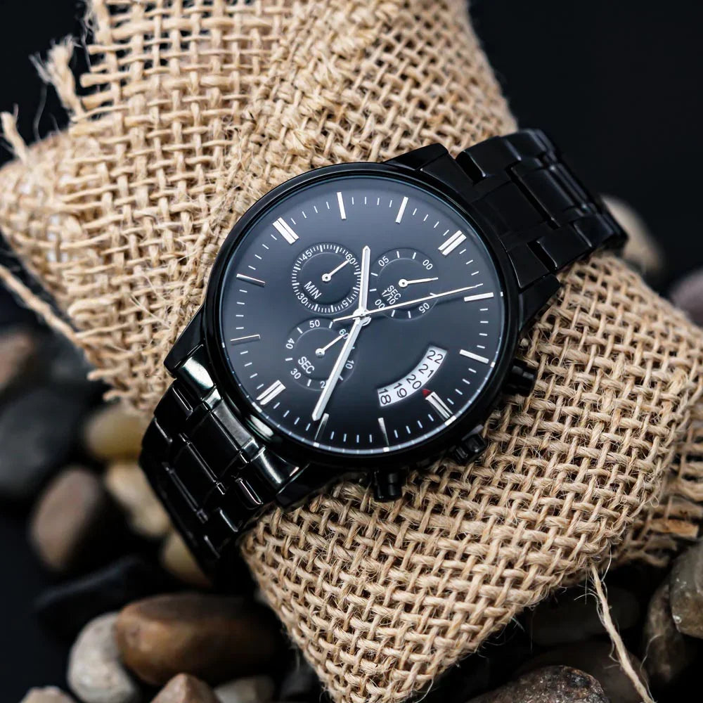Black metal wristwatch with chronograph and date display on burlap cushion surrounded by stones