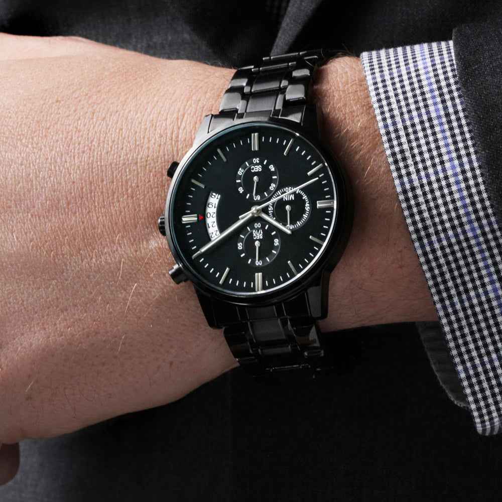 Close-up of a black metal wristwatch with multiple dials worn on a wrist with a black checkered dress shirt sleeve