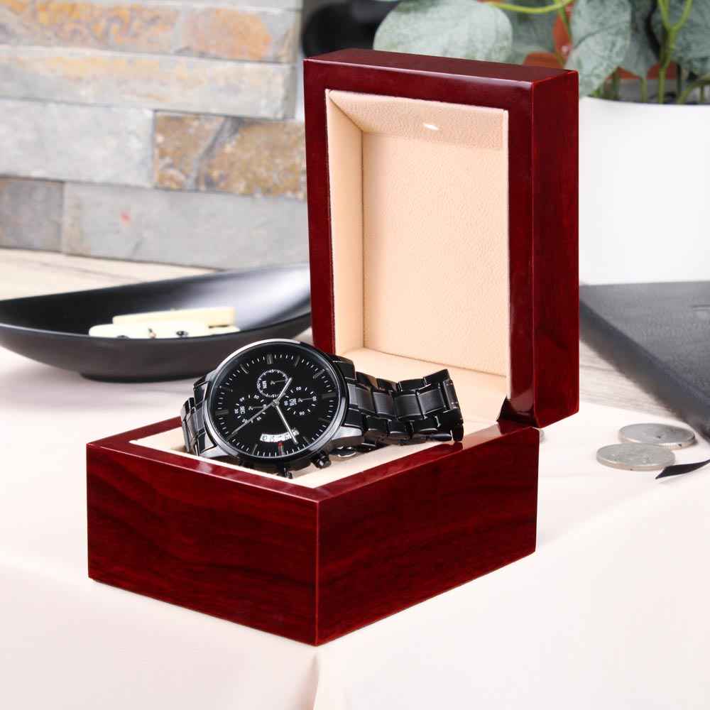 Black metal wristwatch with chronograph features in an open polished wooden display box