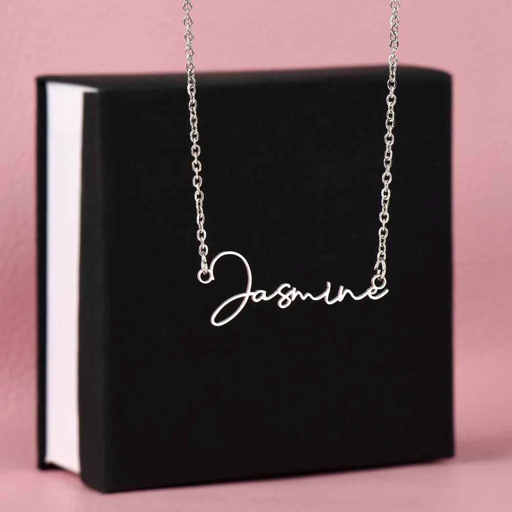 Silver name necklace with cursive 'Jasmine' pendant displayed on black box against pink background