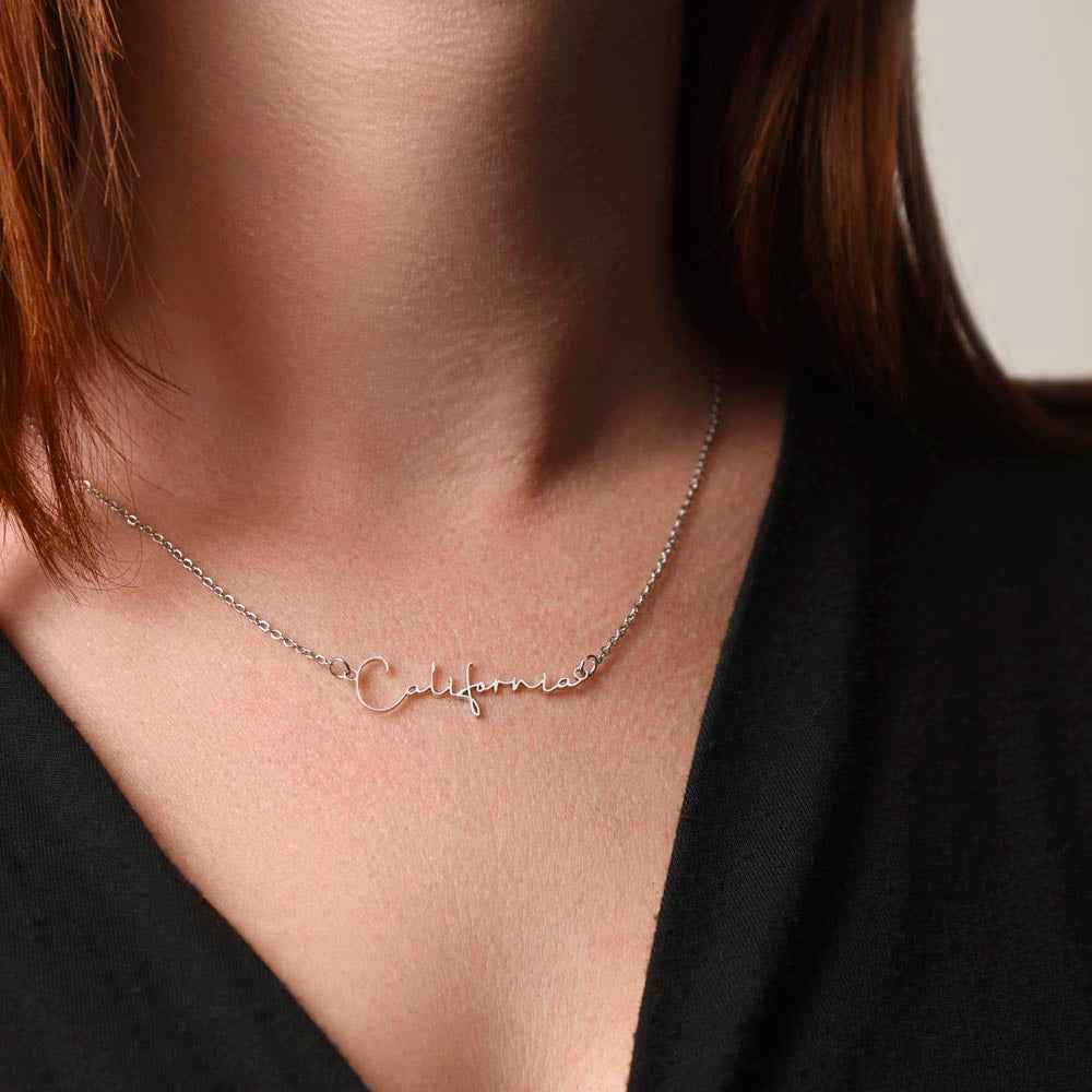 Close-up of a silver California script necklace worn on a woman's neck with a black top