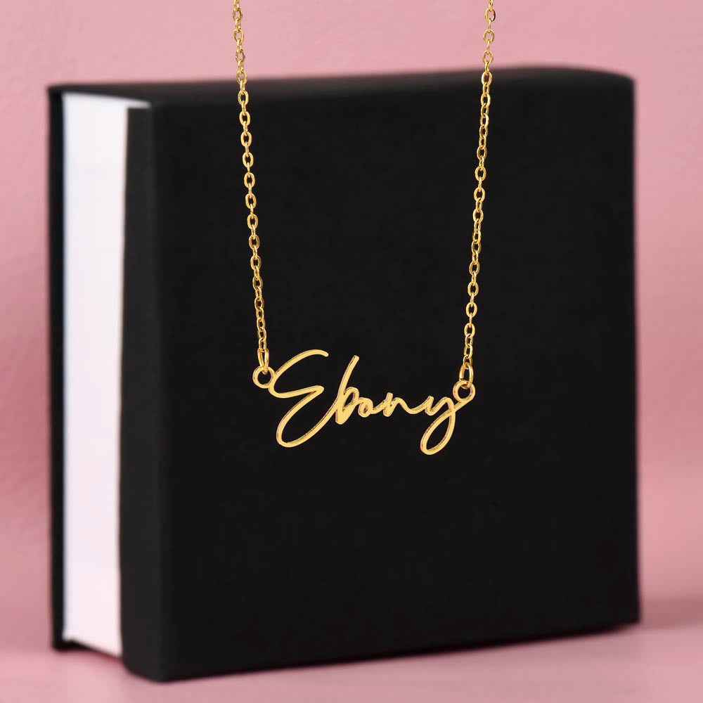 Gold chain necklace with custom name pendant Ebony displayed on black jewelry box against pink background