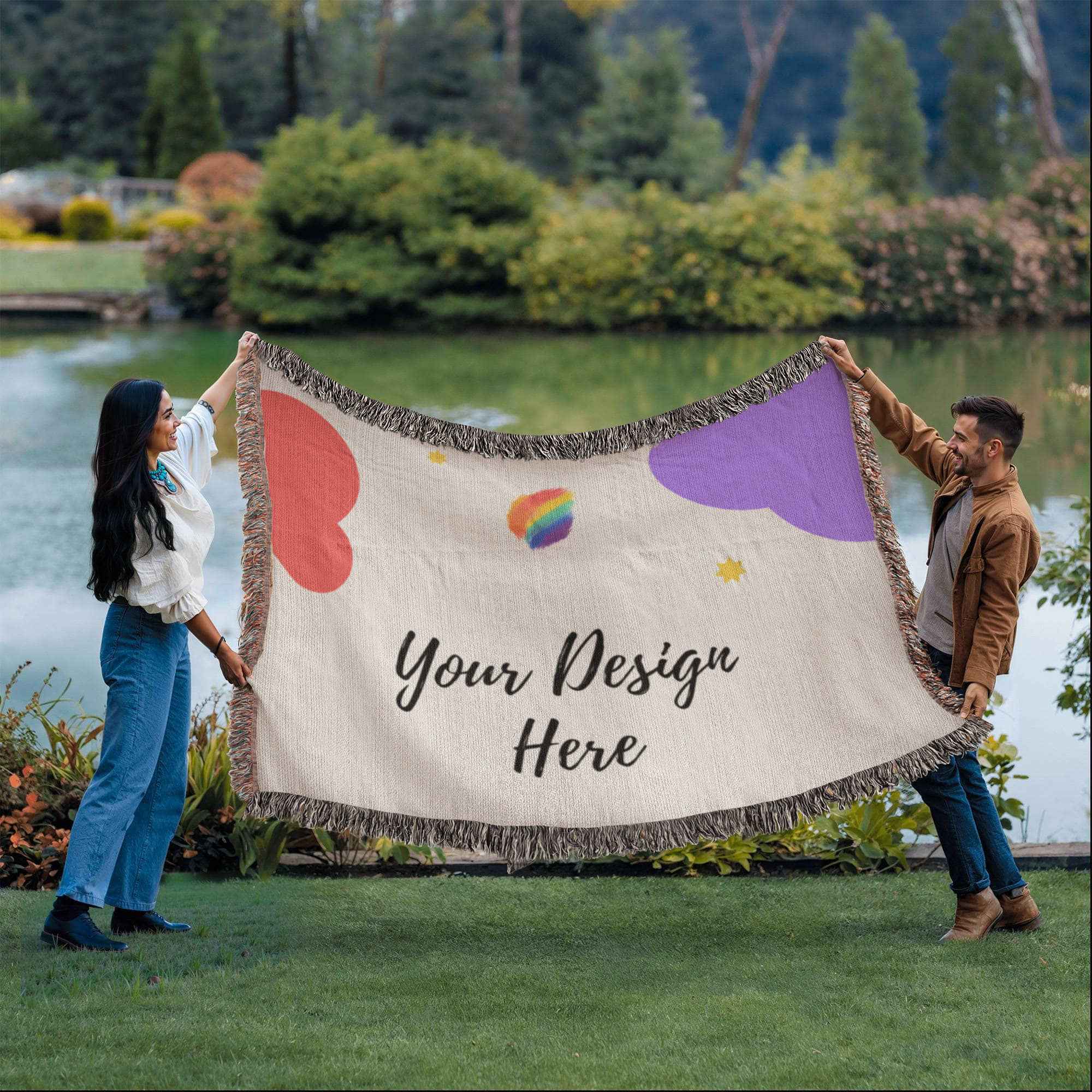Man and woman holding a customizable blanket with heart and rainbow designs by a lake