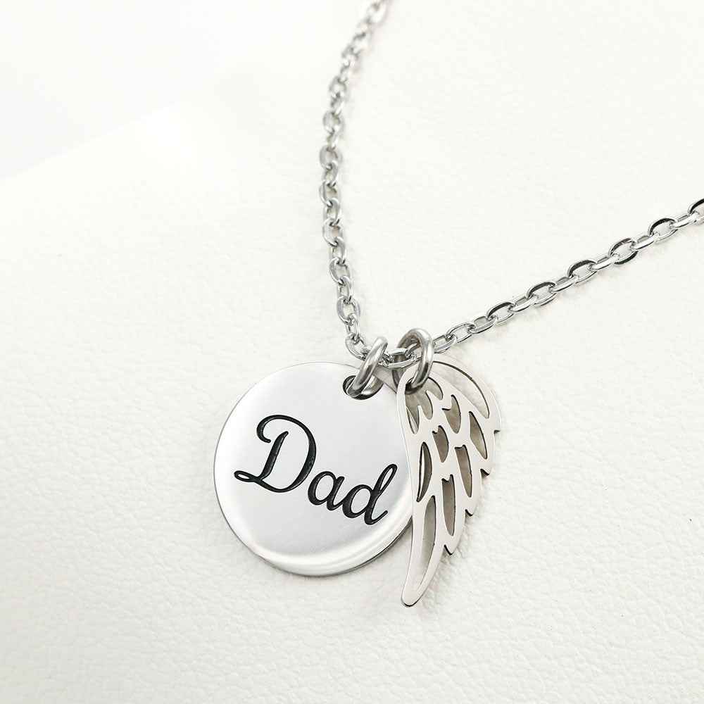 Silver pendant necklace with engraved 'Dad' disc and angel wing charm on white background